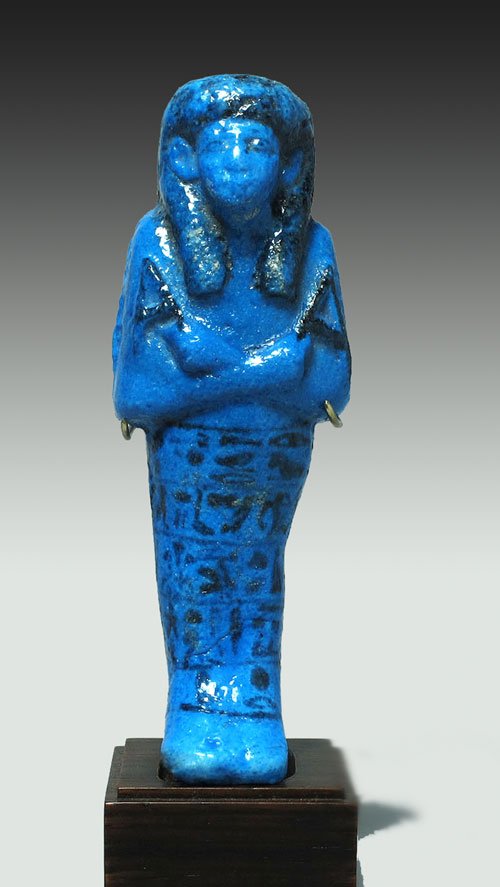 Egyptian Blue Faience Ushabti of Asetemkhbi: Third Intermediate Period, 21st Dynasty, ca. 1070-935 B.C. A fine, large example, bright blue in color with dark manganese details; shabti depicted mummiform with hands folded over chest, holding a ho