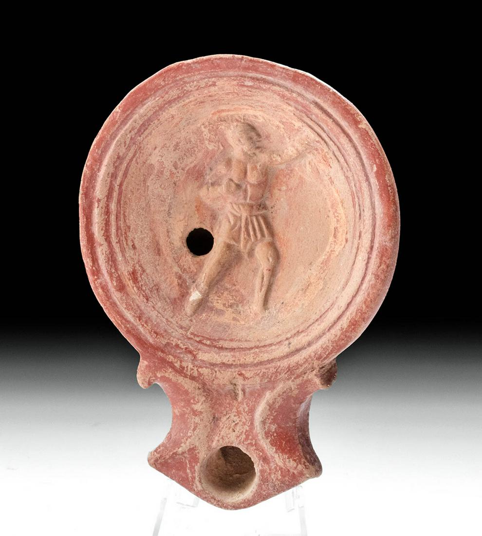 Roman Terracotta Oil Lamp w/ Male Figure Relief Tondo: **First Time At Auction** Rome, Imperial Period, ca. 1st to 4th century CE. A wonderful redware oil lamp presenting a discoid body with a recessed central tondo, petite fill hole, and flared and point