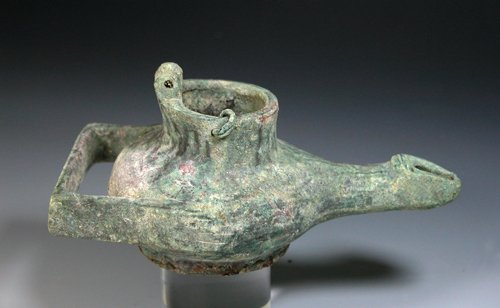 A Late Roman / Byzantine Bronze Oil Lamp: Dating between 400 and 600 AD. Solid bronze vessel with rounded body, long thin spout; rectangular handle ending on each side with human hands with clearly delineated fingers and thumb, filling spout 