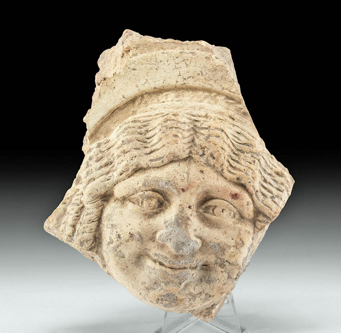 Greek Terracotta Gorgoneion Antefix Fragment: Magna Graecia, South Italic Colonies, ca. 4th century BCE. A mold-made earthenware antefix depicting a Gorgoneion or the head of a Gorgon - a frightening beast-like female creature seen as early as th