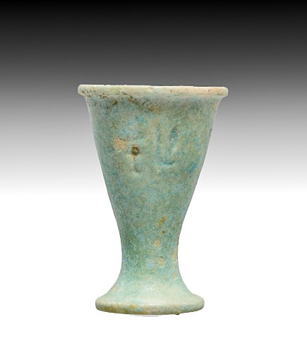 An Egyptian Faience Votive Cup: New Kingdom, 18th-20th Dynasty, 1550-1070 B.C. Glazed faience composition vessel, light blue-green in color, narrow cylindrical body tapering to a conical footed form, with incised hieroglyphic inscri