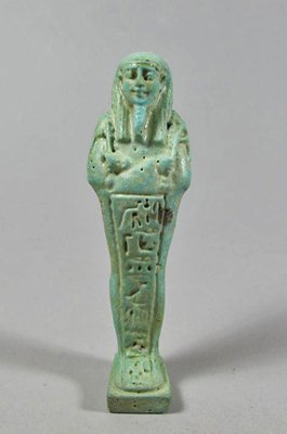 An Egyptian Green Faience Ushabti of Irthyherou: Late Dynastic Period, 712-343 B.C. Green faience ushabti wearing a striated tripartite wig and holding a hoe in each hand plus a seed bag slung over his left shoulder. The front with a vertical column