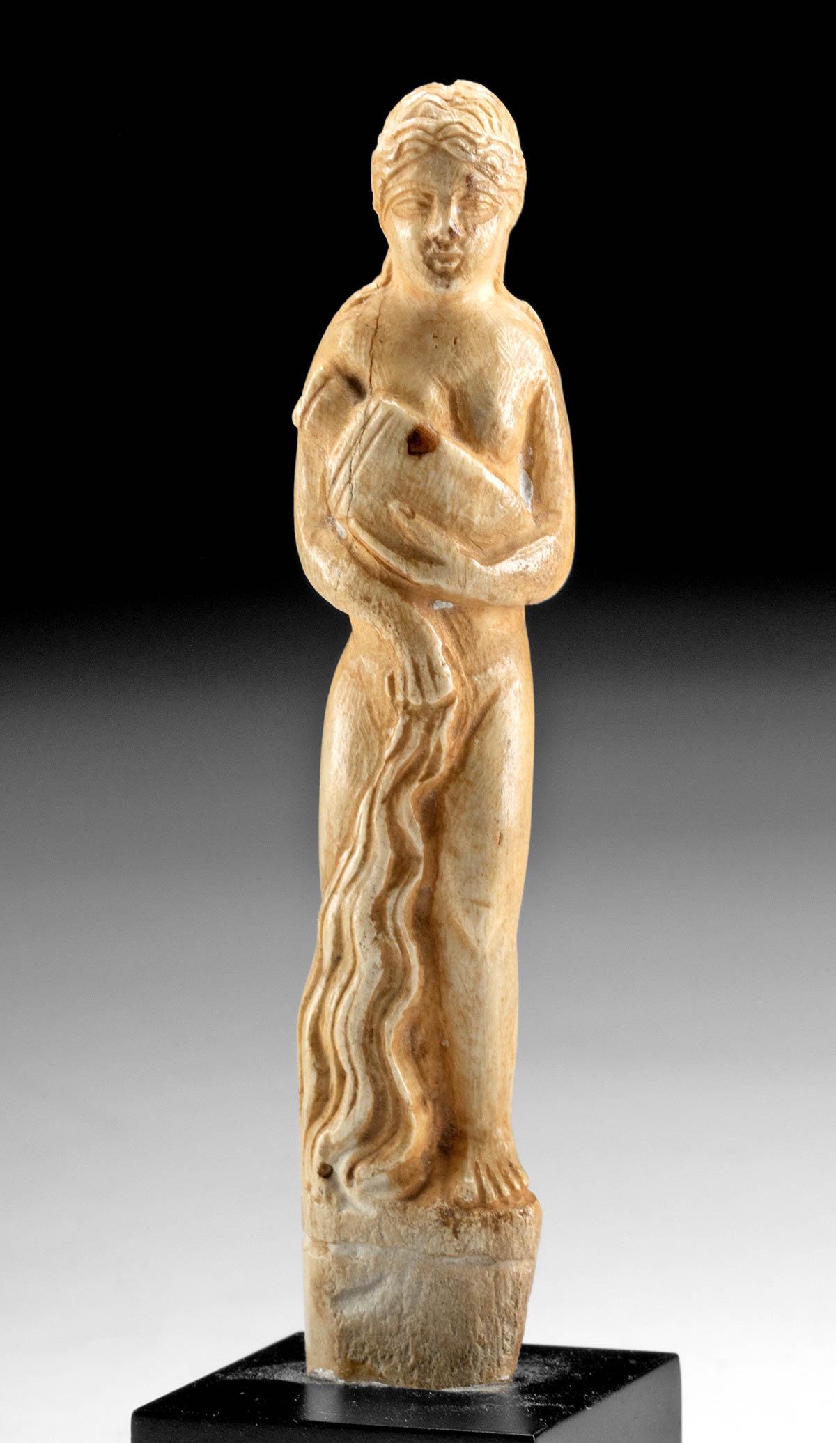Late Roman Bone Carving of a Woman w/ Jar: Roman, late Imperial to early Byzantine Period, ca. 4th to 6th century CE. A beautiful sculpture of a woman, likely the Roman goddess Venus, meticulously hand-carved from the bone of an ungulate. Boas