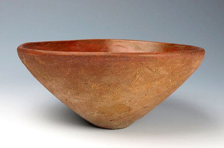 An Egyptian Pre-Dynastic Redware Vessel, Naqada II: Egypt, ca. 3400 to 3200 BC. Of rounded form, the sides of the vessel are smooth and taper toward a narrower, flat base, the rim is rolled and slightly flared. Interior is coated with a thin red iron-o