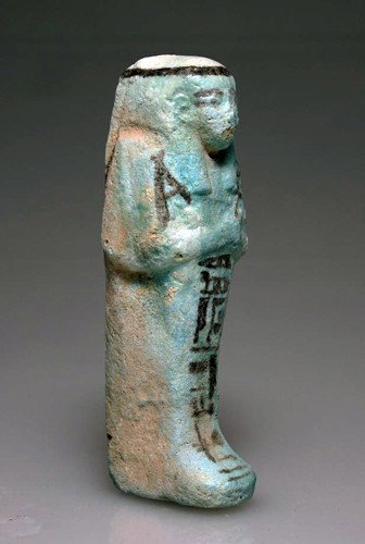 An Egyptian Glazed Faience Shabti: Egypt, 21st Dynasty. Pale blue faience composition ushabti with details in added black, frontal inscription reading "The Osiris, god's father of Amun, Padikhonsu, true of voice;" holding two hoes, wea
