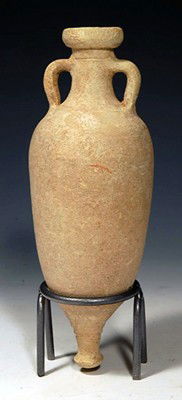 A Graeco Roman Pottery Transport Amphora: Ca. 1st Century BC/AD. A slender terracotta vessel with twin handles, pointed base and cylindrical neck with reinforced rim. 8¼"H(21cm) + stand. there is NO RESERVE on this lot