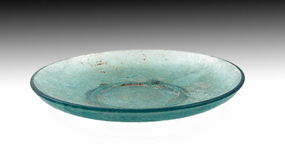 A Late Roman to Byzantine Glass Plate: Roman to Byzantine (and quite possibly Coptic), dating between 400 and 700 AD. Lovely sea-blue dish of typical form, small foot and moderately concave surface. 5-1/8"D. Provenance: Found in Jerusalem.