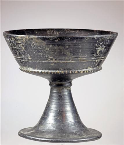 An Etruscan Bucchero Chalice : Etruria, ca. 7th Century B.C. Etruscan Bucchero pottery chalice on a flared stem; bowl decorated with horizontal fans above two incised encircling bands, with a notched ridge below. Size: 16 x 14,5 cm