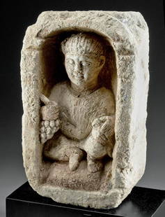 Romano-Egyptian Limestone Stela Boy Holding Dove: Romano-Egyptian, Late Imperial to Coptic Period, possibly Antinoe, ca. 4th century CE. A magnificent limestone funerary stela of a boy seated in a niche grasping a dove in his left hand and a bunch