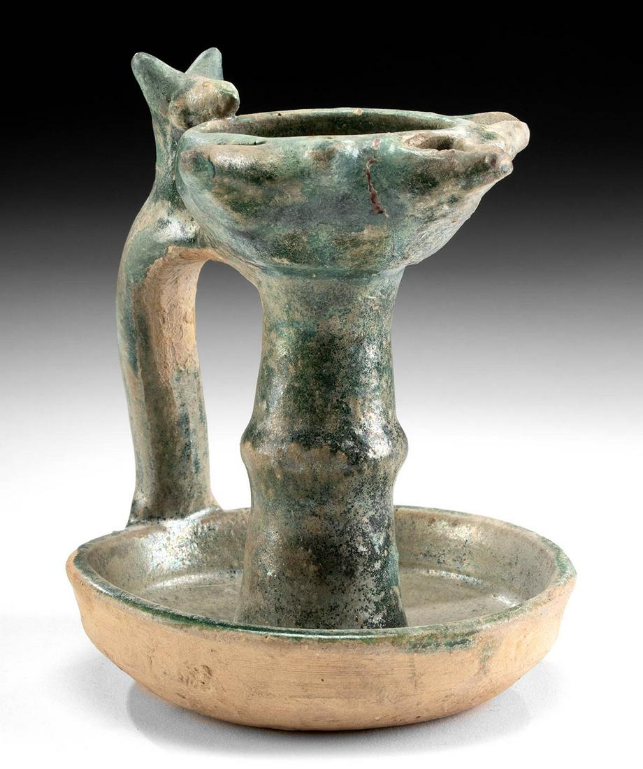 12th C. Persian Nishapur Glazed Pottery Oil Lamp: Near East, Persia (Iran), Nishapur area, Islamic culture, ca. 12th to 15th century CE. A stoneware oil lamp that rests on a shallow saucer shaped base that acts as a drip pan to catch overflow. A thic