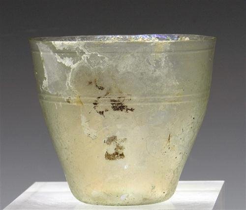 A Roman Glass Beaker / Goblet: Rome, ca. 200 AD. Pale green glass drinking vessel of slightly flaring form, with three bands of lathe-cut circumferential decoration just under rim and mid-body. The base is slightly kicked up and th