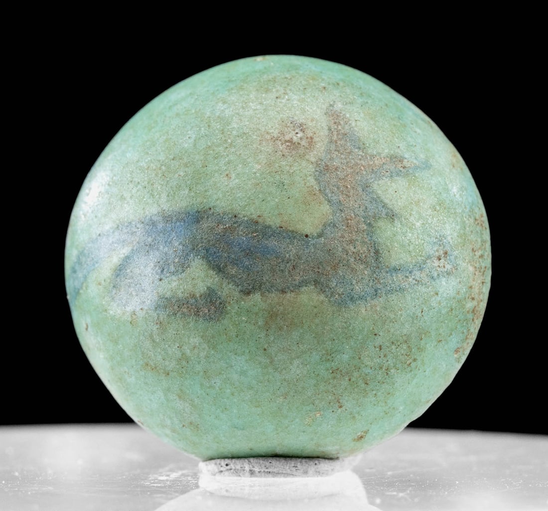 Published Egyptian Faience Cabochon Recumbent Jackal: Ancient Egypt, Late Dynastic to Ptolemaic Period, ca. 664 to 30 BCE. An extremely rare faience cabochon of hemispherical form covered in turquoise-hued glaze, the center bearing a recumbent jackal in 