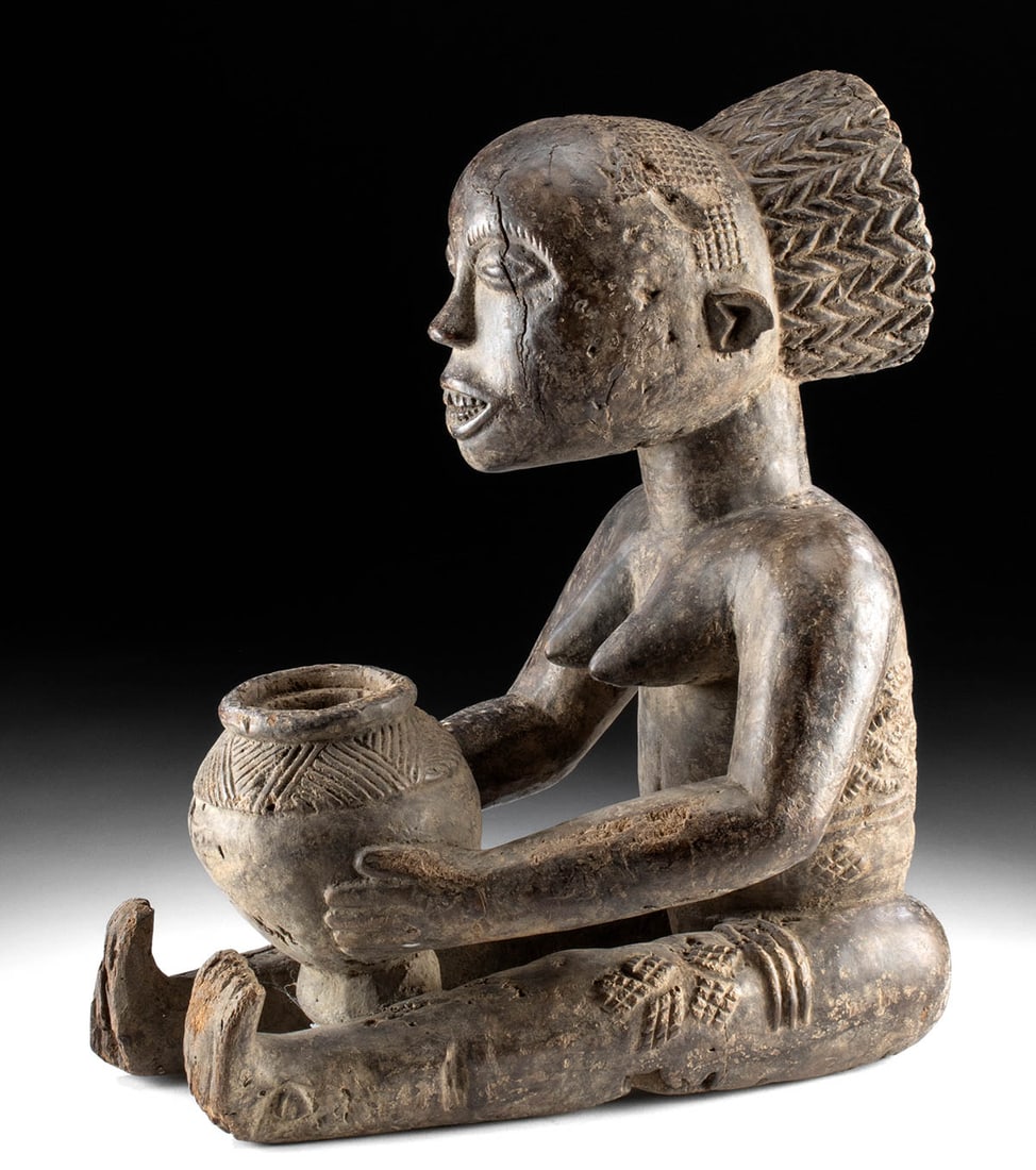 Rare African Luba Nude Female Mboko Bowl Bearer: Central Africa, Democratic Republic of the Congo, Luba peoples, ca. early to mid-20th century CE. A rare example of a female Mboko bowl bearer, shown nude and seated with legs stretched out in front, 