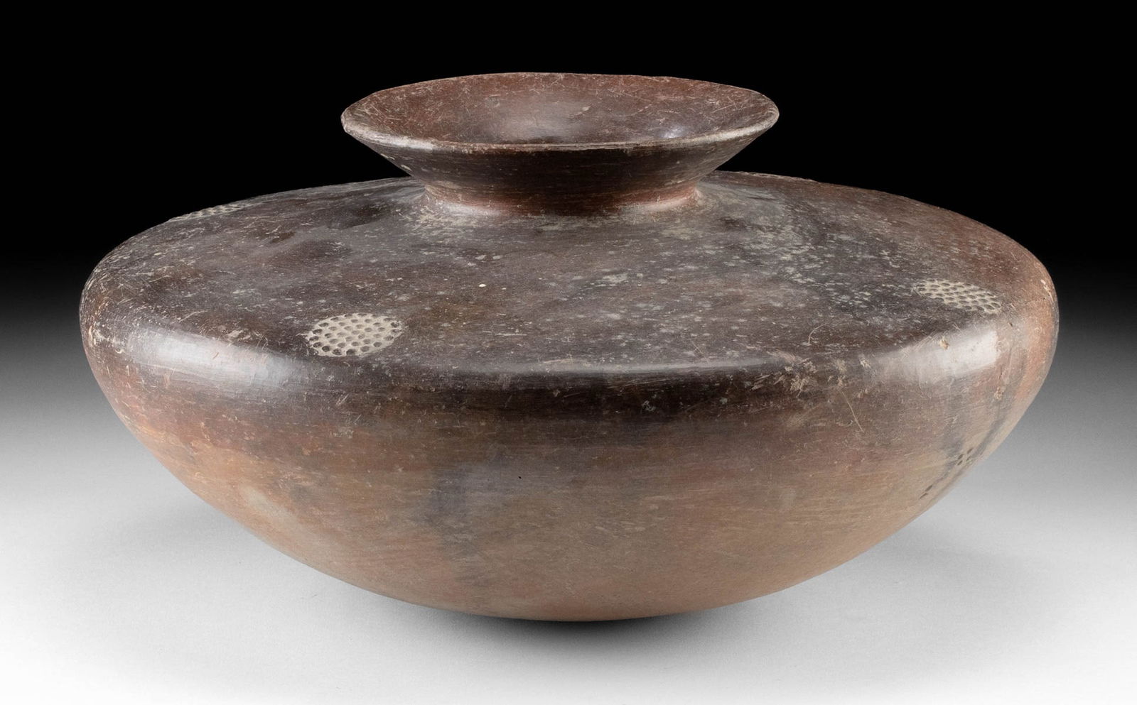 Colima Redware Pottery Squat Jar: Pre-Columbian, West Mexico, Colima, ca. 300 BCE to 300 CE. A hand-built and stone-burnished pottery jar exhibiting a low, wide profile and a dark red hue. A quartet of stippled medallions - perhaps fl