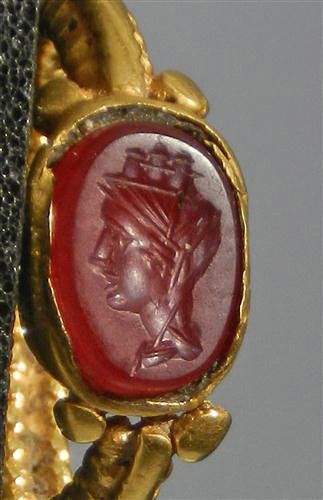 A Roman Carnelian Intaglio Set in Roman Gold Mount: Roman Empire, ca. 200 AD. High karat gold ring (22-24K gold), the bezel with a braided wire surround; the shank with applied beading. The red carnelian intagio gemstone shows the draped and tarred bus