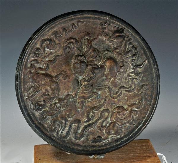 A Chinese Han Dynasty Bronze Mirror: China, ca. 206 BC - 220 AD. Cast bronze, of circular form; face features woman flying amongst geometric shapes in raised relief; rear is undecorated and when polished, reflects image of person looking