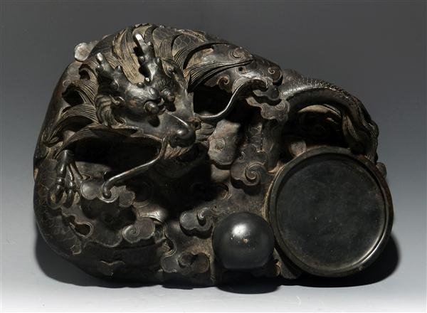 A Chinese Inkstone, Dragon / Pearl Carving: China, Qing Dynasty, (1644-1911). Intricately carved stone, the smooth sunken palette emptying into a circular ink-pool, the top and one side carved with sinuous dragons amid swirling clouds. In addit