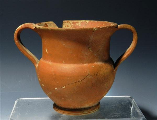 A South Italic Redware Kantharos, Published: Southern Italy, Ca. 5th-4th Century BCE. Large redware jug with two handles on either side, slipped in a reddish orange paint, sits on raised platform. Base and interior remaine the natural color of t