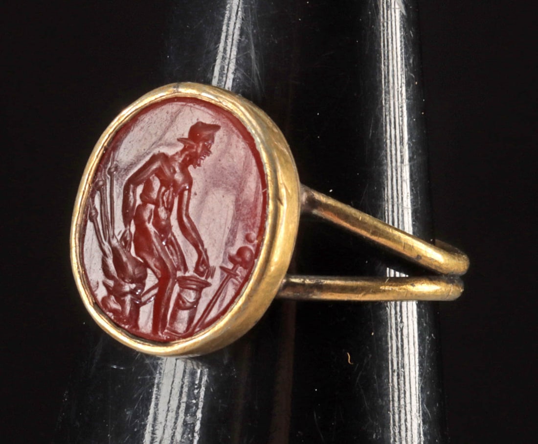 Roman Carnelian Intaglio Nude Helmeted Male (Ring): Roman, Imperial period, ca. 1st to 2nd century CE; Europe, ca. 20th century CE. An attractive Roman carnelian intaglio of a nude helmeted figure before an altar, all set in a modern gilt brass ring to