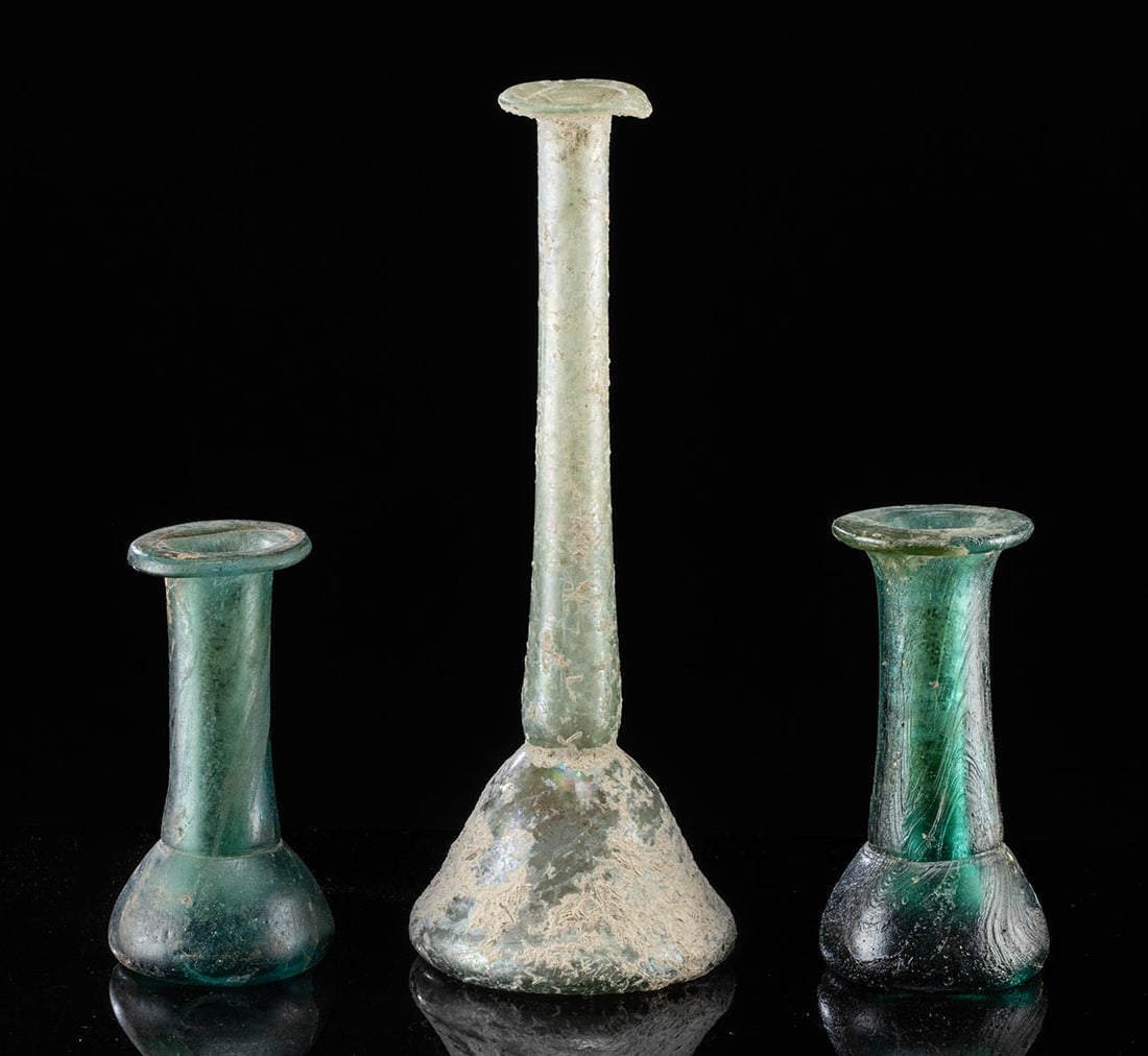 Ancient Roman Glass Flasks (group of 3): Roman, Imperial Period, ca. 1st to 3rd century CE. A trio of glass flasks, including an unguentarium with thin, nearly transparent pale green sides and a concave base. Unguentaria like this were used