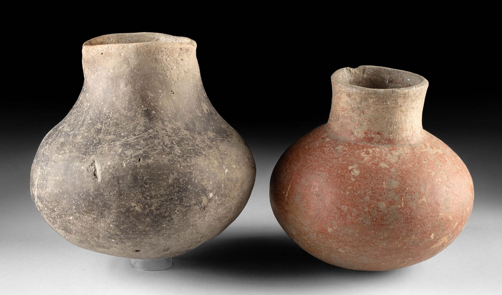 Two Prehistoric Mississippian Pottery Jars: Native American, Southeast or Midwest, Mississippian, ca. 900 to 1543 CE. A lovely pair of pottery jars, one redware and one grayware. Both present piriform bodies with annular rims and a round yet st