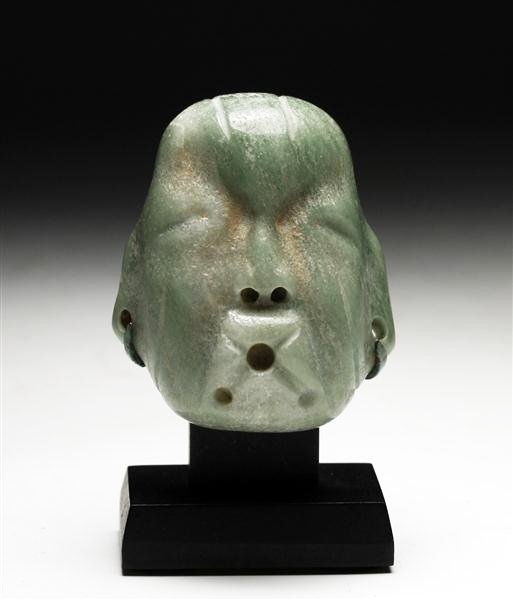 A Pre-Columbian Olmec Jade Maskette: Pre-Columbian, from Southeastern Mexico, Olmec culture, ca 1100 to 500 BCE. Medium-green jade, featuring a "singer" with lips pursed in almost whistling pose, string-cut hair, facial features and dril
