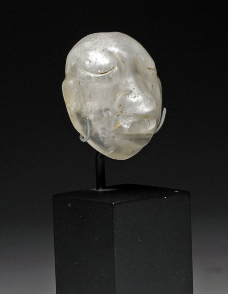 A Pre-Columbian Olmec Crystal Head: Pre-Columbian, Eastern Mexico, Ca 1200 to 500 BCE. Small, clear quartz crystal carved into the form of a human face with exagerated nose and large lips, bi-conical hole drilled in top of head for susp