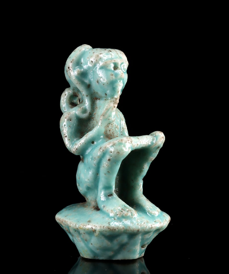 Egyptian Faience Amulet Harpocrates Seated on a Lotus: Egypt, Late Dynastic to Ptolemaic period, ca. 332 to 30 BCE. A delightful and quite rare faience amulet depicting the child-god Harpocrates seated on a lotus flower with one finger of his right hand p