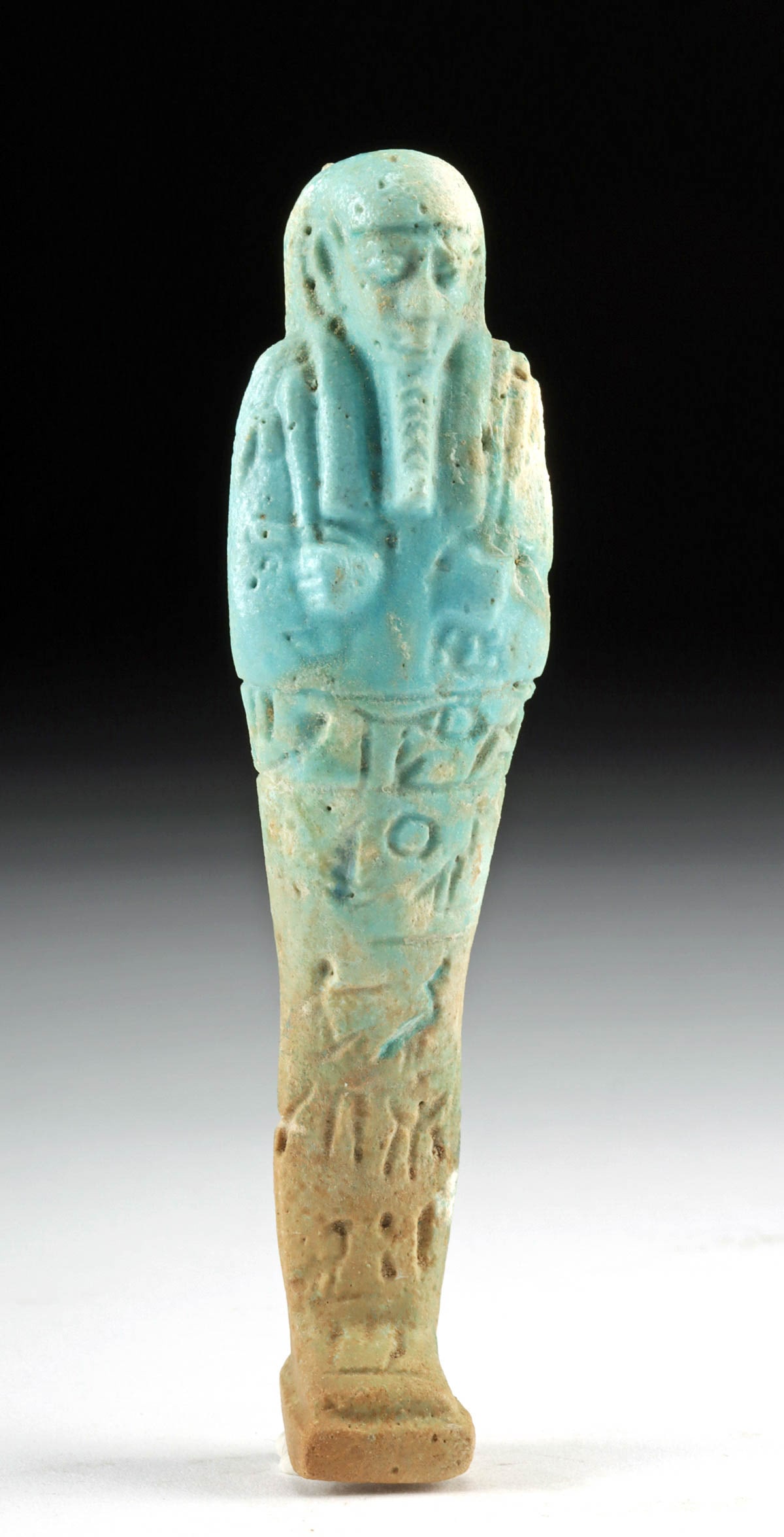 Egyptian Faience Ushabti w/ Hieroglyphs: Egypt, Late Dynastic to Ptolemaic period, 26th to 33rd Dynasty, ca. 672 to 30 BCE. A lovely faience ushabti standing mummiform a top a plinth and holding a pick and a hoe with a seed bag on his back,