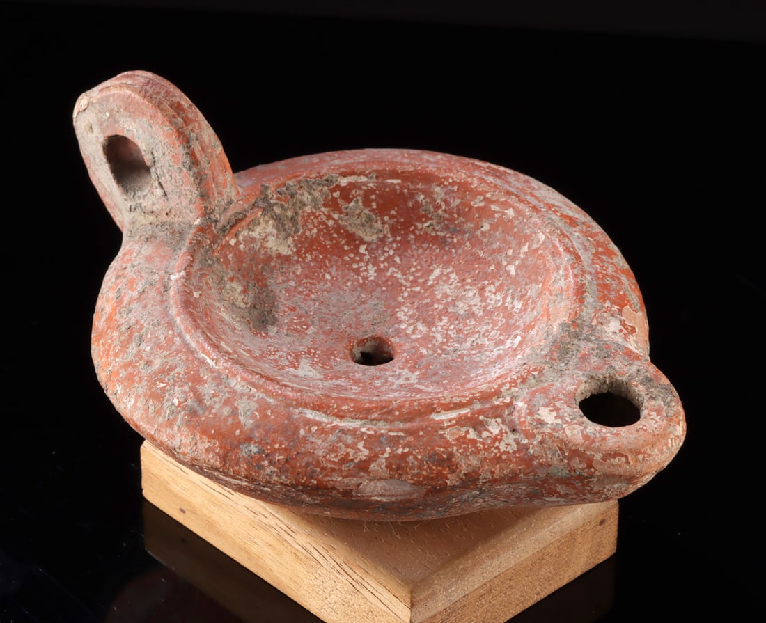Roman Pottery Oil Lamp: Roman, North Africa, Imperial period, ca. 1st to 3rd century CE. A wonderful redware oil lamp of discoid form with a recessed central tondo, a rounded spout, a narrow fill hole, and a loop handle, all