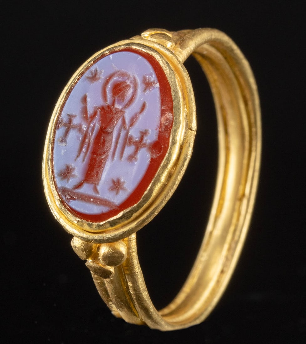 5th C. Byzantine Gold Ring w/ Glass Intaglio Saint Orans: Ancient Near East, Byzantine period, ca. 5th to 6th century CE. A stunning gold ring mounted with a glass intaglio of a saint, perhaps the Virgin Mary, in the orans pose with both arms raised. Crowned
