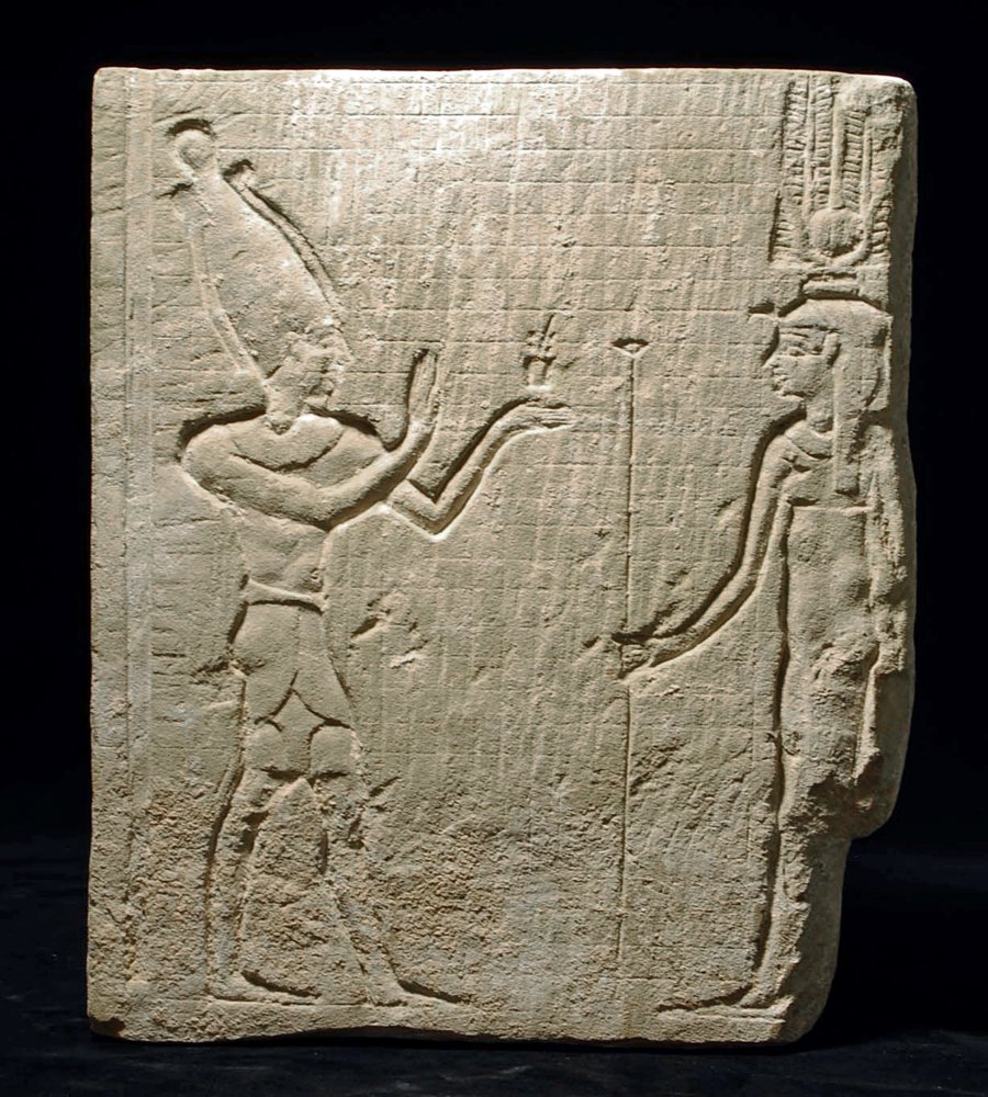 An Egyptian Limestone Carved Relief - Osiris and Isis: Egypt, Late period, ca. 700 to 30 BC. Squared section of light colored limestone showing a full figure of the striding Osiris at left. He wears the crown of Upper Egypt, a knee-length kilt and extends