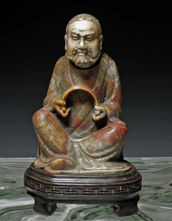 A Magnificent Lohan Chinese Buddha Protector: China, Qing Dynasty, Ca 10th century. Exceedingly detailed stone carving of a seated Lohan - one of there 18 Chinese protectors in Buddhist temples. Shown with knees raised upwards wearing an extremel