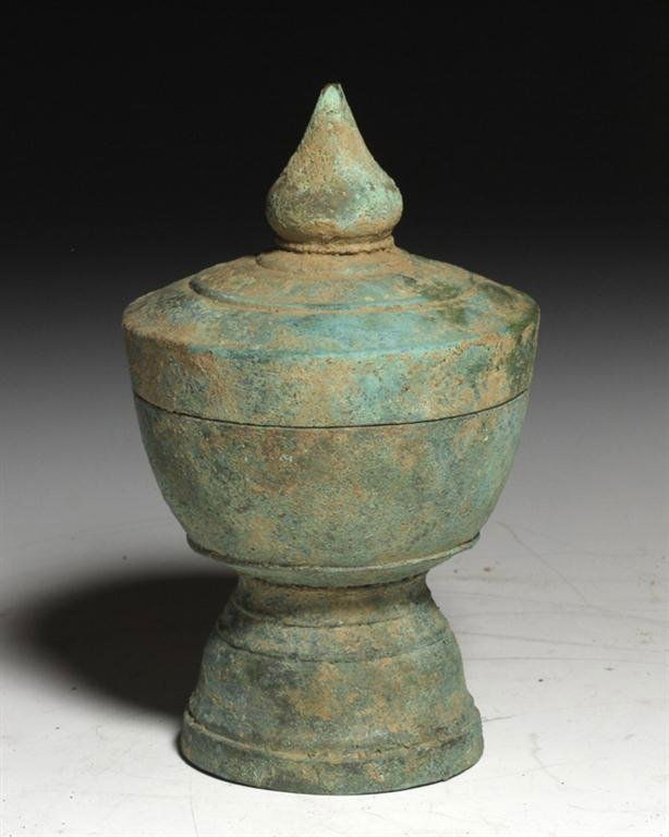 A Thai Lidded Bronze Pyxis: Thailand, 12th century CE. Delicate and quite refined bronze covered vessel, most likely used to hold lime powder. Deep foot with three decorative rings, lid with bulb-shaped terminal and twin decorat