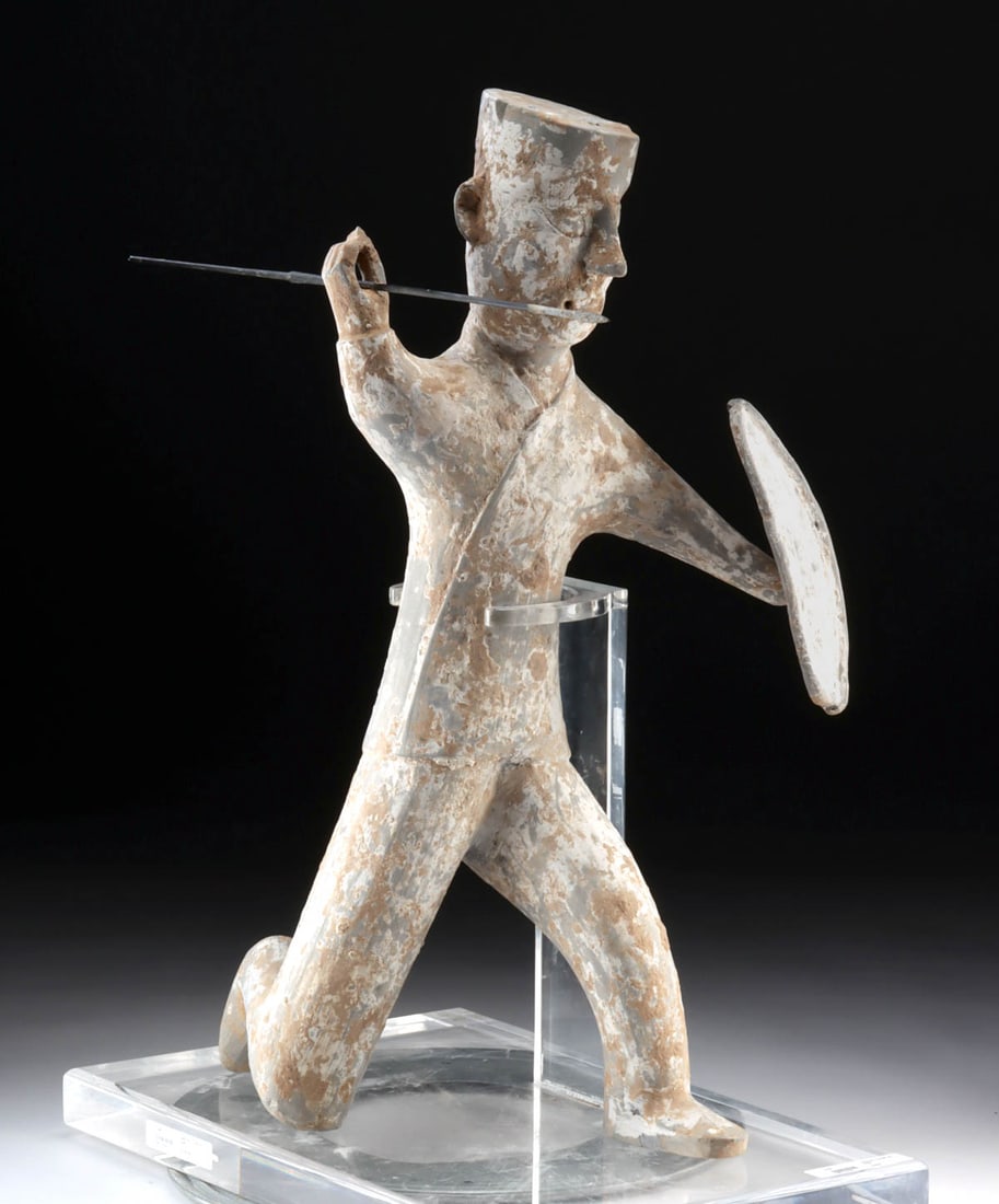 Chinese Han Pottery Warrior Figure w/ Spear & Shield: East Asia, China, Han Dynasty, ca. 206 BCE to 220 CE. A dramatic pottery figure of a warrior donning a metal spear in one hand and a shield in the other as he prepares to attack, leaning back on his b