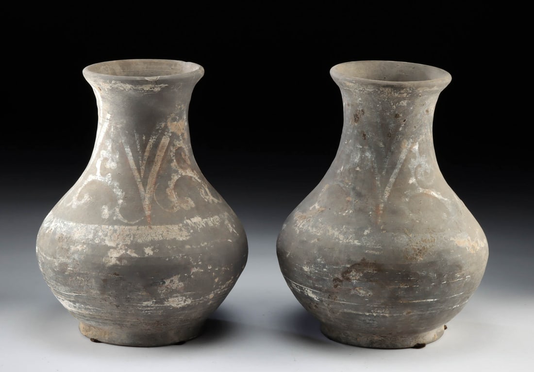 Pair of Chinese Han Dynasty Painted Pottery Hu Jars: East Asia, China, Han Dynasty, ca. 206 BCE to 220 CE. A fabulous pair of grayware jars, each presenting a piriform body with a flared rim, all sitting up on a ring-shaped foot. Liberal remains of whit