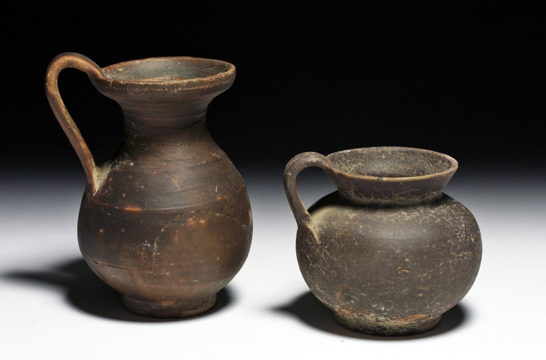 2 Published Greek / Daunian Blackware Pottery Jugs: Southeastern Italy, Ca 4th century BCE. Two pottery blackware pouring vessels uncovered in a Daunian tomb in 1944 by Byron Farwell, and later (1953) published in a book on his collection. First, an ol