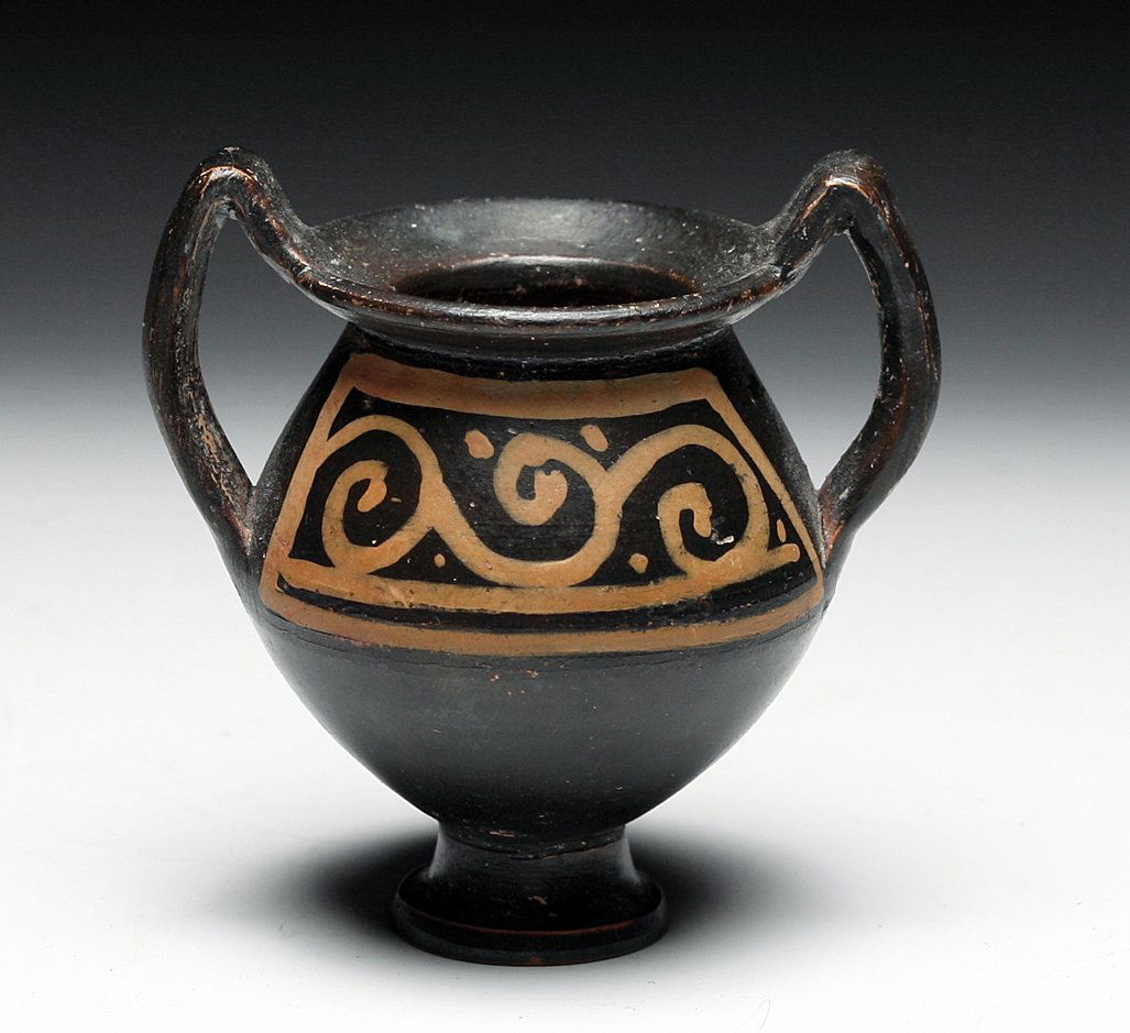 A Greek Xenonware Miniature Amphora: Magna Graecia, Ca. 5th-4th Century BCE. A miniature Xenon pottery amphora stands on a raised pedestal and has two high handles. Painted red design on both sizes, one side featuring a stiff linear desi