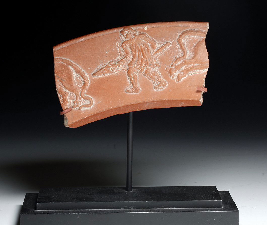 A Roman North African Pottery Fragment - Gladiator: North Africa, ca 300 to 400 CE. Nice section of a large redware vessel decorated in deep relief with a standing gladiator holding a long spear, lion to each side of him. 5"W. Custom base PROVENANCE: E
