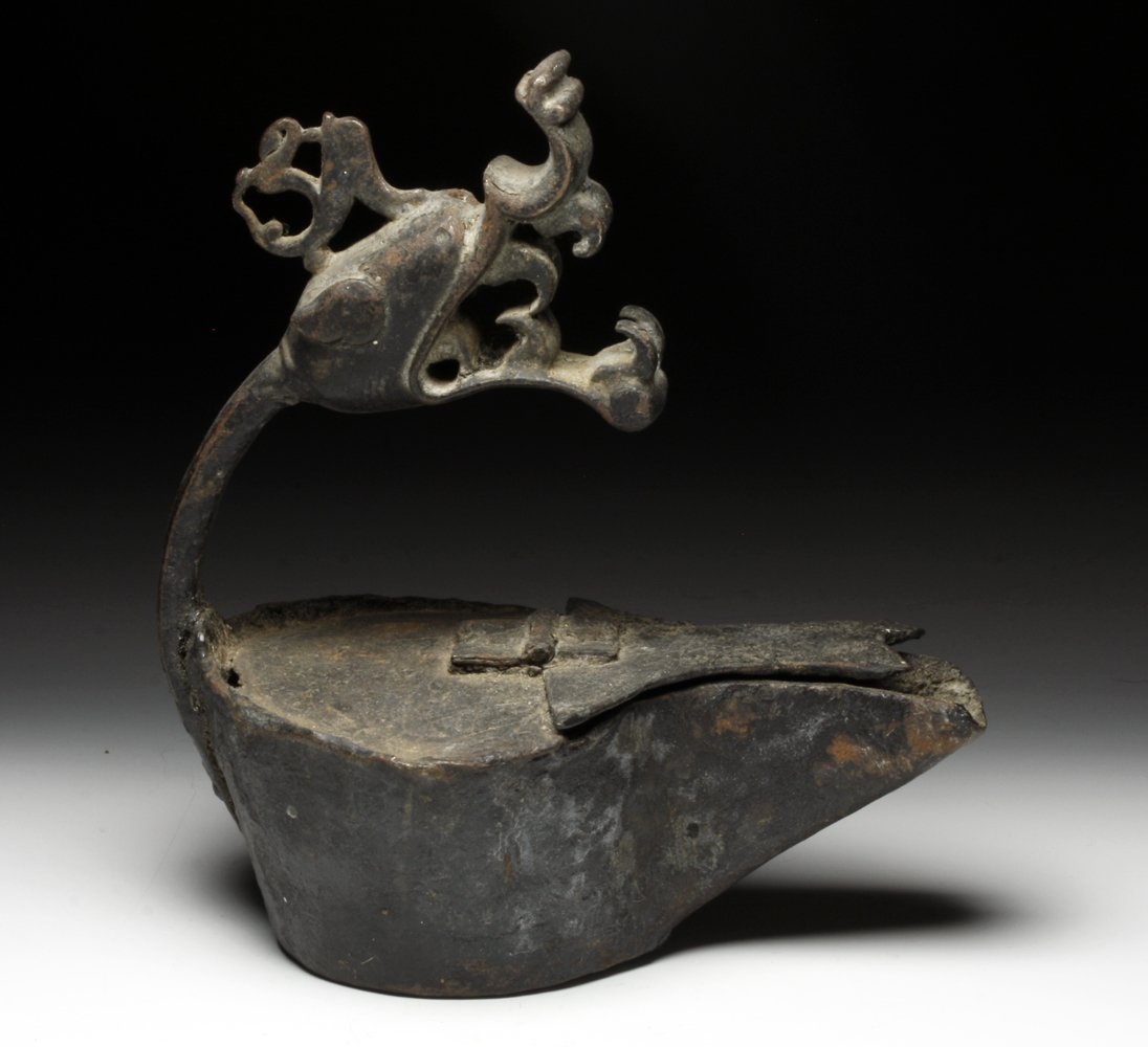 A Tibetan Bronze Oil Lamp - Dragon Form: Tibet, ca. 17th to 18th century. Unusual oil lamp of squarish form, handle terminating in the head of a snarling dragon - mouth open and large toothy grin greeting the user. Provenance: Ex-Sarkisian E