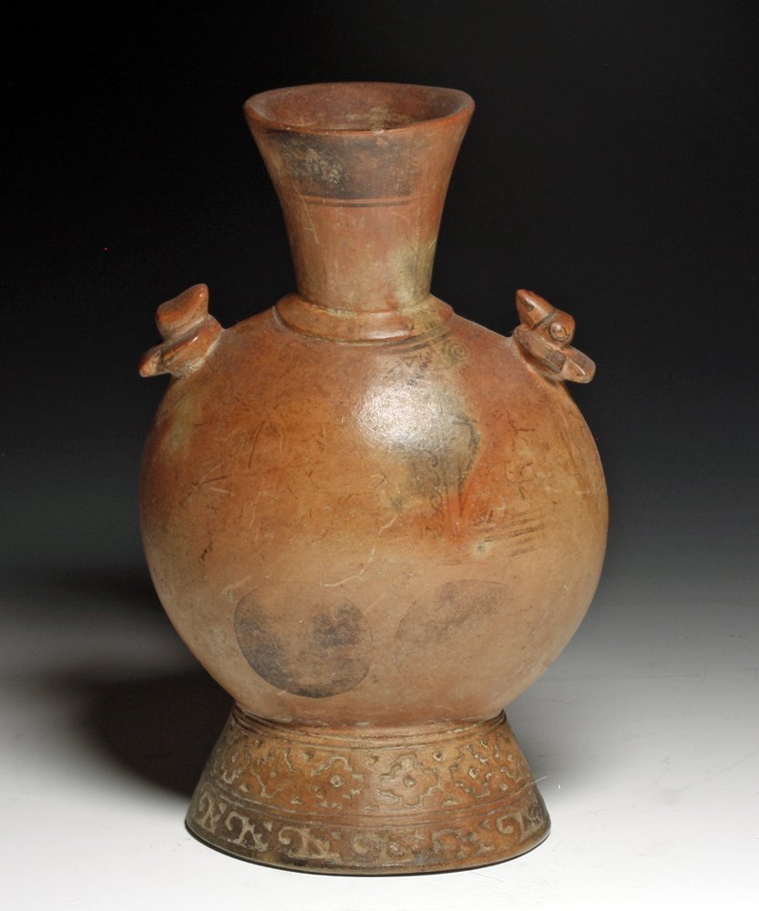 Pre-Columbian Lambayeque / Sican Pottery Jar: North Coastal Peru, Ca 800 to 1100 CE. Redware pottery jar on sloped oval foot, canteen-shaped body and slightly flring rim, strap handle connecting body to rim. Base is decorated with impressed "Inca
