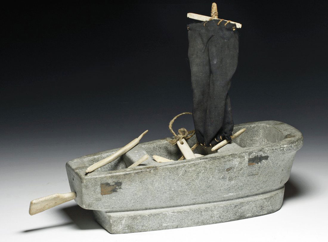 An Eskimo Soapstone Carving - Boat & Tools: Canadian, Inuit, acquired in the 1950's. Large soapstone boat with sail and a number of carved walrus ivory implements - including gun, oars, harpoon, rudder, etc. 10" L by 9" H to top of sail. PROVE
