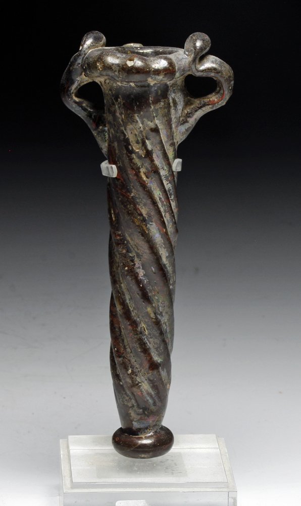 Islamic Coreform Glass Vial: Middle East, Ca. 7-9th Century CE. Stands on raised glass base, carved glass lines on body create an illusion of twisted glass, as well as a nice textured grip. Two handles on either sides of the roun