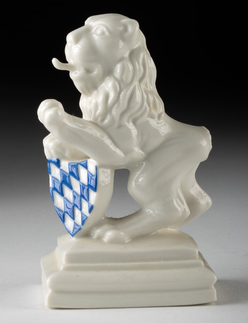 Nymphenburg German Porcelain Lion Coat of Arms Figurine: Western Europe, Germany, ca. late 20th to 21st century CE. A glazed Nymphenburg porcelain heraldic lion holding a white shield painted with blue-and-white lozenges, the coat of arms associated with th