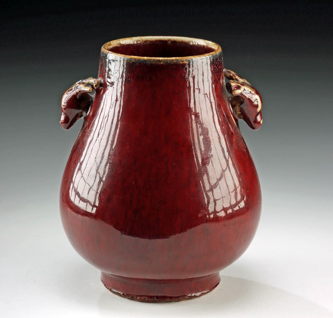 Qing Porcelain Hu Vase - Sang de Boeuf w/ Stag Handles: East Asia, China, Qing Dynasty, ca. 19th to early 20th century CE. A refined porcelain hu vase enveloped in a deep sang de boeuf (ox blood) glaze, its surface shimmering with a rich, variegated crimso