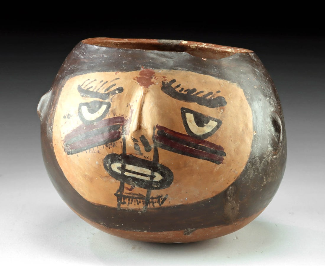 Nazca Pottery Decapitated Portrait Head Vessel: Pre-Columbian, South Coast Peru, Nazca culture, ca. 200 to 600 CE. A powerful polychrome pottery vessel in the form of a human trophy head, the rounded body modeled as a severed head with boldly paint