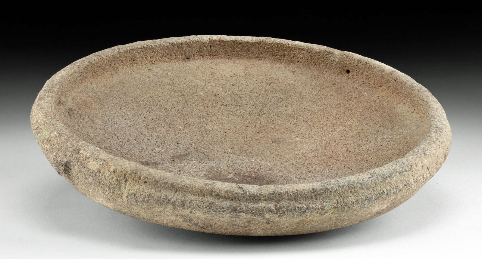 Cypriot Late Bronze Age Basalt Dish / Mortar: Ancient Mediterranean / Near East, Cypriot, Late Bronze Age, 1600 to 1000 BCE. A shallow stone dish carved from a single piece of basalt with a low rim. A pair of large notches on both sides of the ex