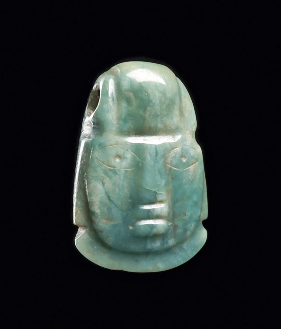 Olmec Jade Head Pendant: Carved blue-green jade head pendant having relief carved and incised facial features, wearing a tightly fitted dome shape cap. Biconical drilled suspension hole in the upper portion of head. Intact, e