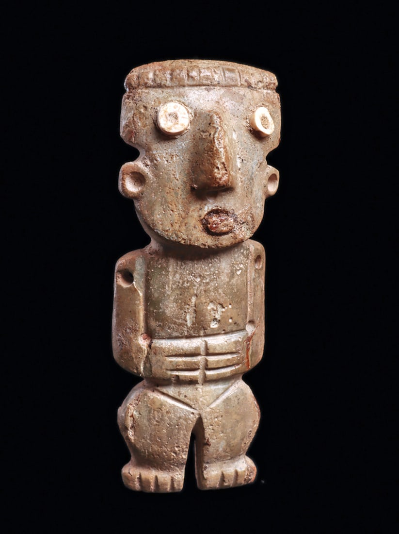 Chontal Standing Stone Figure with Inset Eyes: Carved grayish-green serpentine stone standing figure holding his hands across his stomach, delineated fingers, wide hips. Relief carved angular nose, applied disc shell eyes. Angular shoulders with a