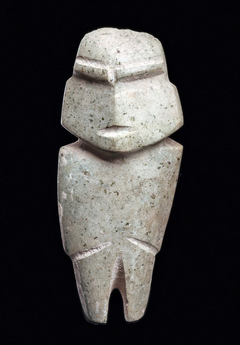 Guerrero Serpentine Standing Figure: Carved light bluish-green serpentine standing idol, having a tapered head with angular facial features, heavy browline, recessed eyes and narrow open mouth. Arms indicated with diagonal lines, angular